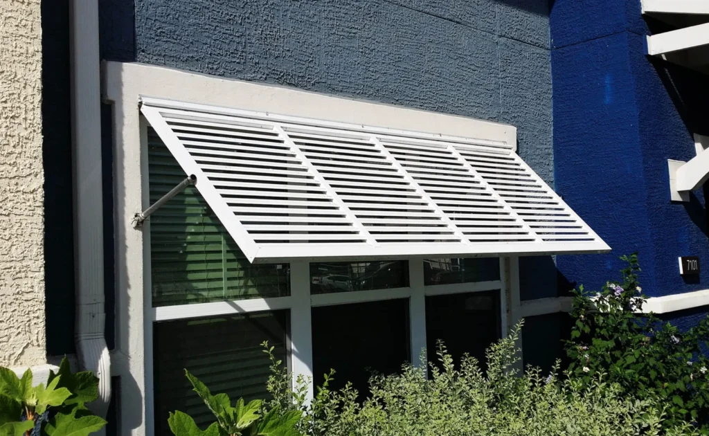 White aluminum Bahama shutter sunshade over a window on a dark blue wall