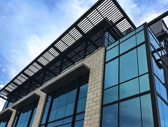 Black aluminum rooftop trellis above the glass curtain wall of an office building
