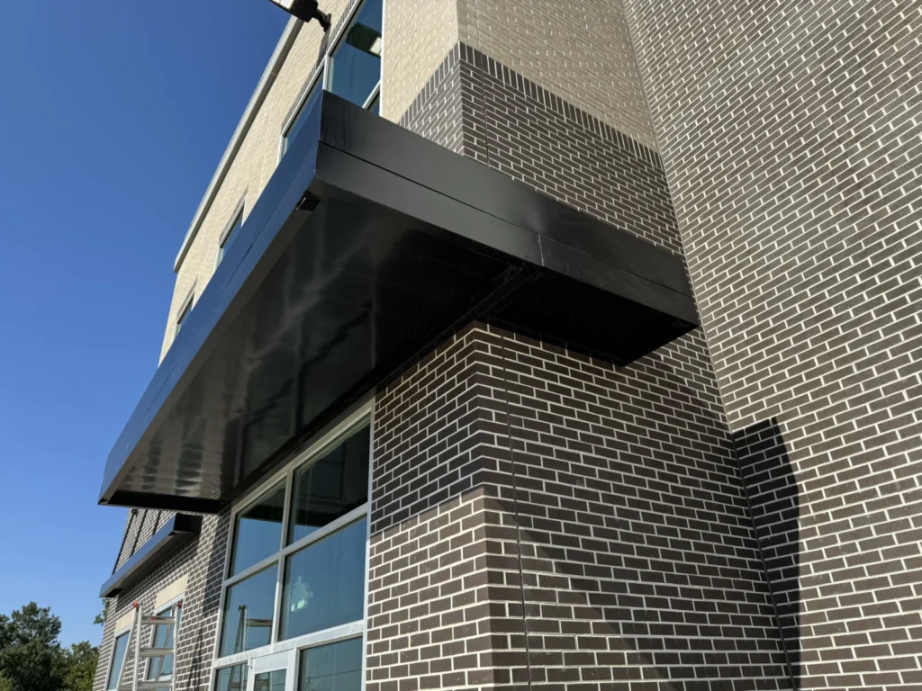 Dark aluminum canopy wrapping the corner of a brick building